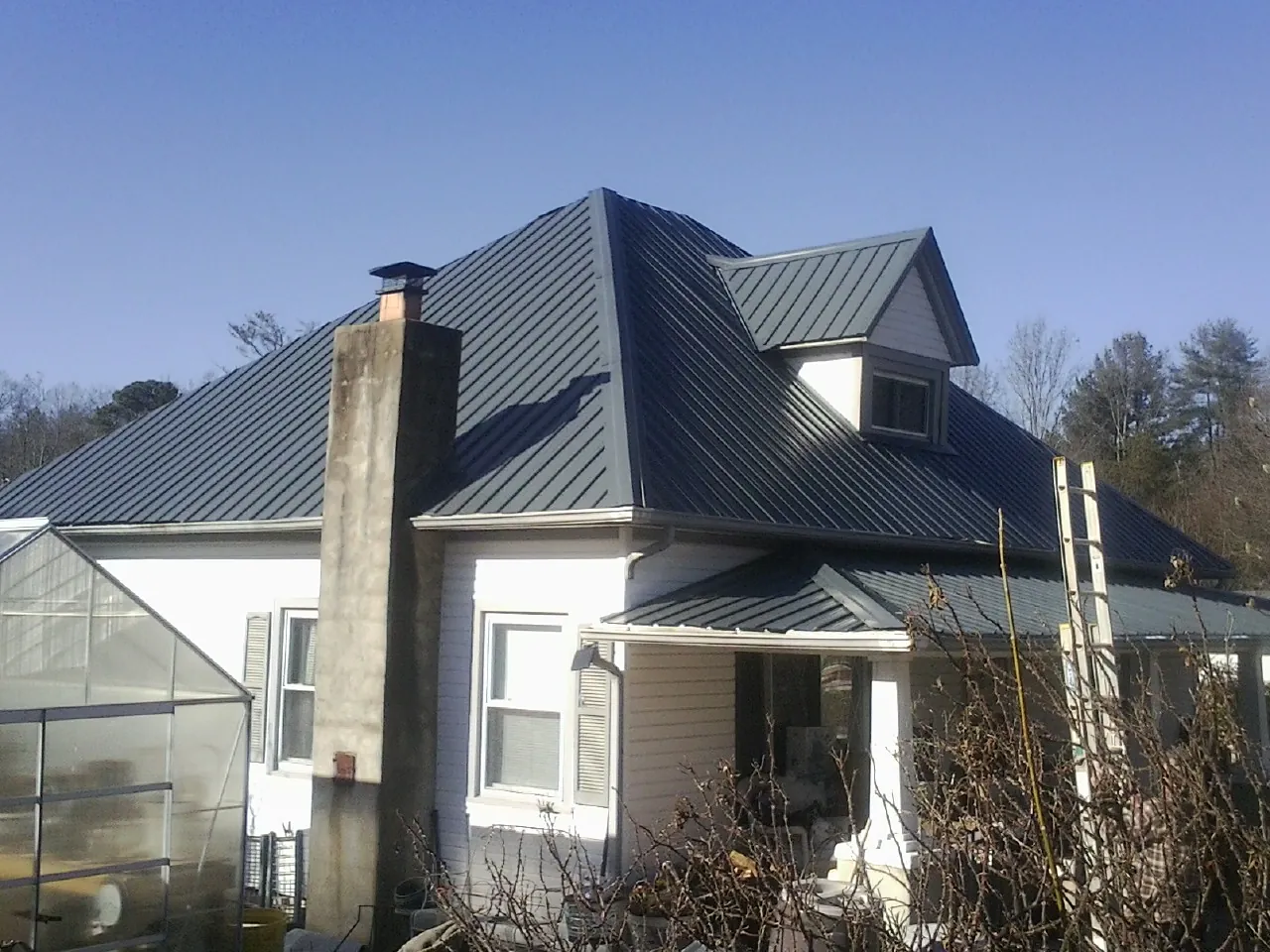 Dark blue standing seam metal roof on a white farmhouse with dormer — Slate & Tile Roof Repair by Roofing Brothers in Grapevine