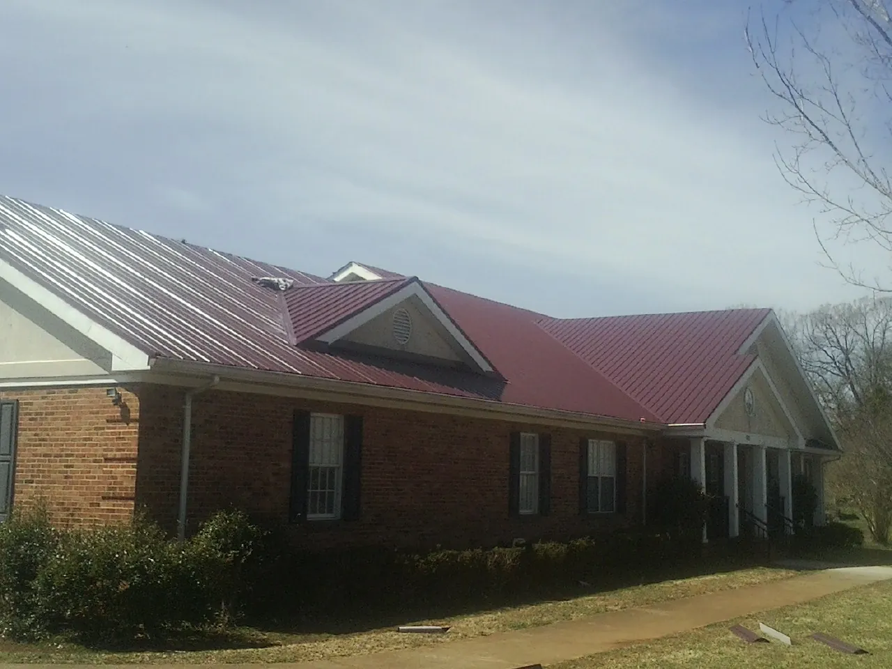 Red metal roof with gabled entries on a long brick building, from a Hail Damage Roof Repair job in Grapevine