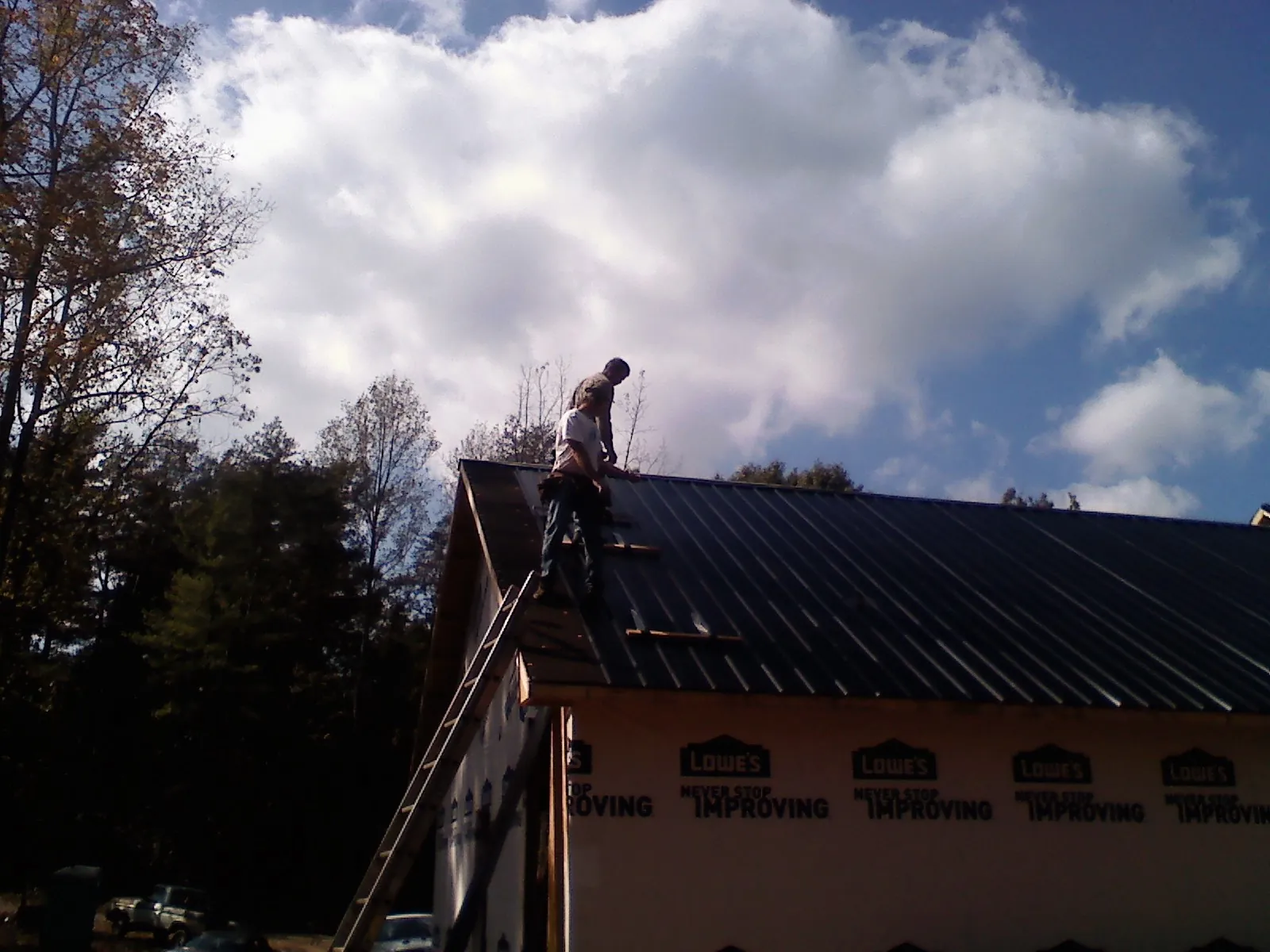 Roofer fastening dark metal panels high against a cloudy sky, from a Roof Inspection job in Grapevine