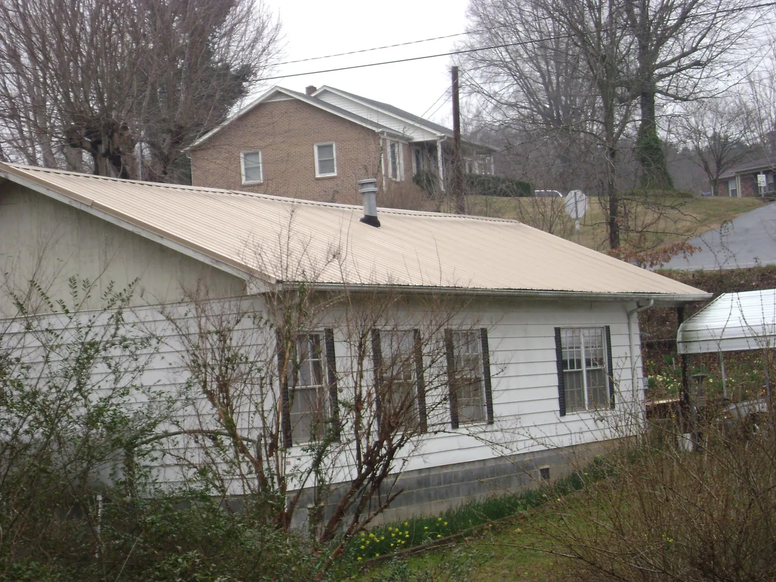 Tan metal roof on a white sided house set into a hillside — Commercial Roofing by Roofing Brothers in Grapevine